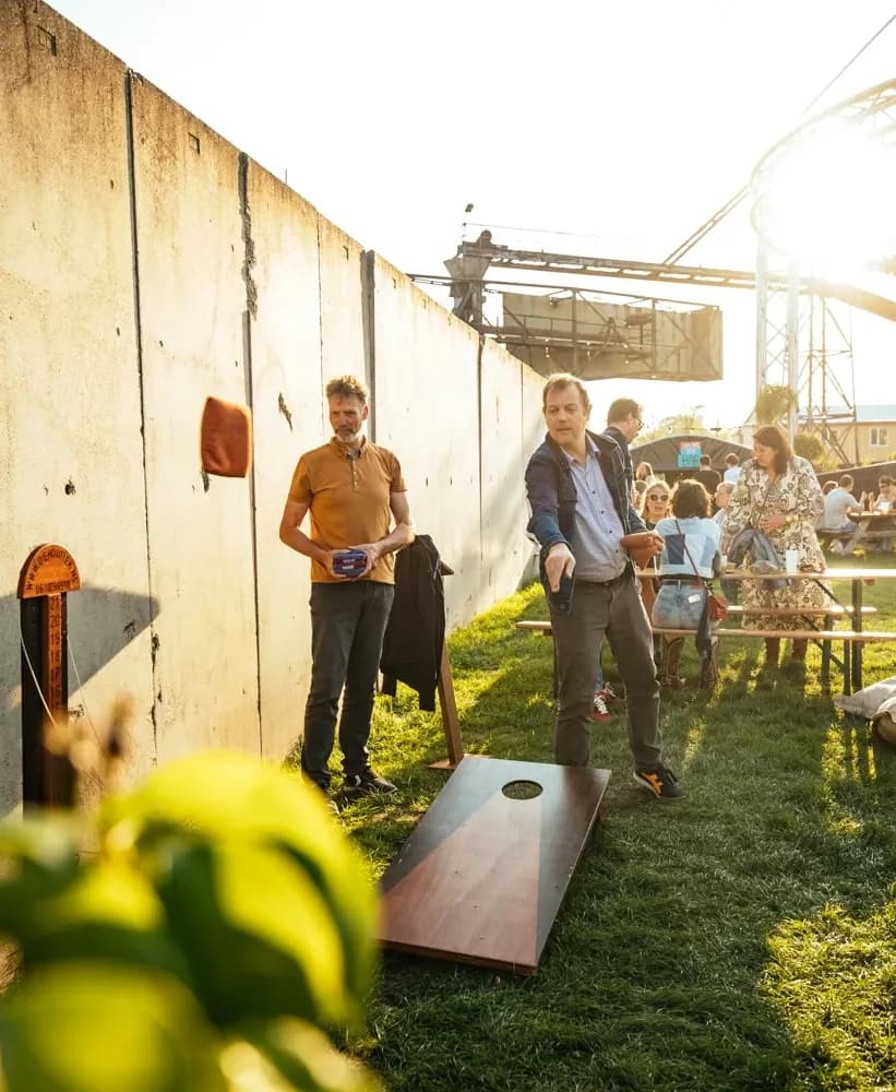 Twee mannen gooien zakjes naar het cornholebord langs een betonnen muur